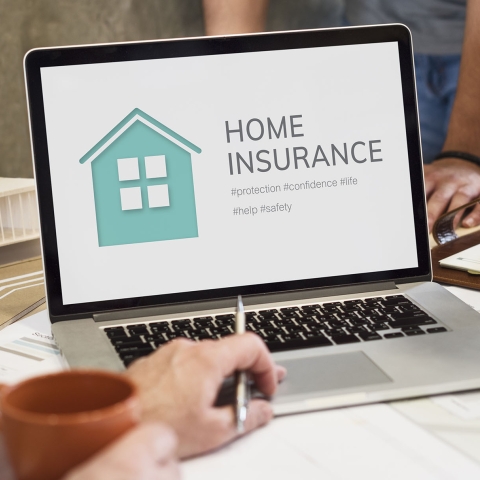 The words Home Insurance appear on a laptop computer screen as a hand uses the mousepad